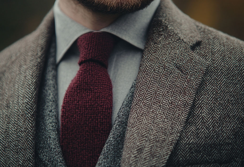 man wearing a gray herringbone tweed sport coat with a white oxford cloth button down shirt and a maroon knit tie