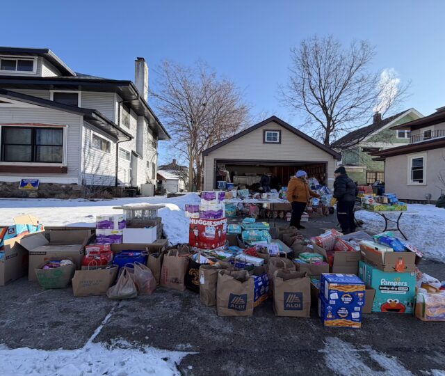 Many bags and boxes of household goods and groceries spilling out of a garage and onto the driveway and sidewalk.
