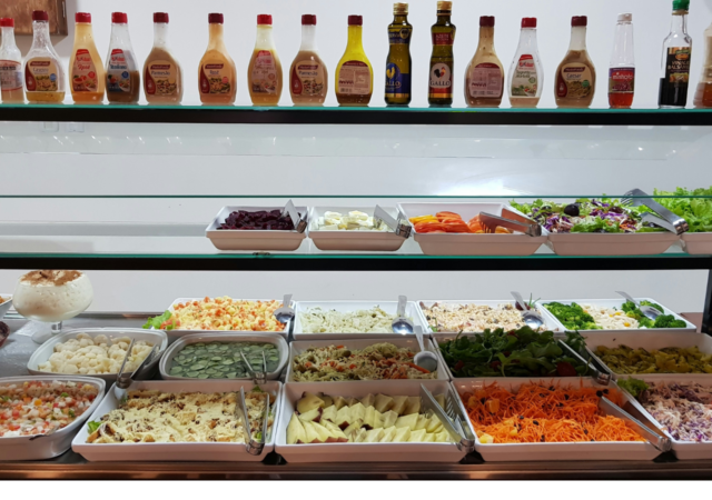 A self-serve salad bar with a variety of fresh vegetables, prepared salads, and dressings.
